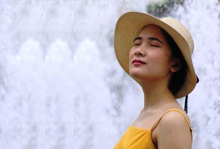 Photo d'une femme vêtue d'un chapeau de paille élégant ferme les yeux et écoute le bruit de l'eau d'une fontaine clapoter.